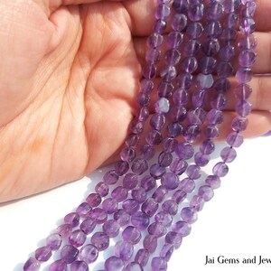 May include: Multiple strands of faceted, coin-shaped purple amethyst beads. The beads exhibit varying shades of translucent violet and are strung together in long, continuous lines, showcasing a polished, reflective surface texture throughout.
