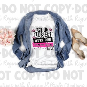 May include: White t-shirt with black and pink graphic text that reads "Get in Loser We're Doin Dance Mom Stuff". The graphic has pink lips and a black splatter effect. The t-shirt is laid out on a white surface with a denim jacket, a bouquet of pink roses, and two pairs of beige shoes.
