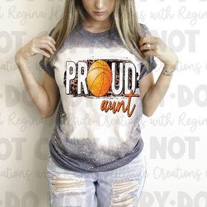 May include: A gray and white bleached t-shirt with a distressed graphic of a basketball and the text "Proud Aunt". The graphic has a leopard print background.