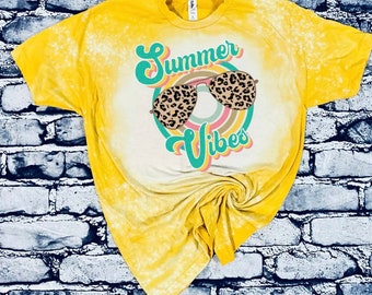 Puede incluir: Camiseta amarilla con diseño decolorado. La camiseta presenta el texto "Summer Vibes" en una fuente retro, con gafas de sol con estampado de leopardo. Un estilo casual de verano.