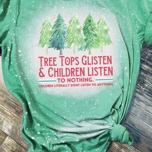 May include: Green t-shirt with a bleached effect and a graphic of five stylized Christmas trees. The text reads "TREE TOPS GLISTEN & CHILDREN LISTEN TO NOTHING. CHILDREN LITERALLY DONT LISTEN TO ANYTHING."