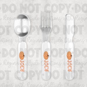 May include: A set of three pieces of children's silverware: a spoon, fork, and knife. Each piece has a white handle with an orange pumpkin graphic and the name "Joey" in orange. The spoon and fork are silver.