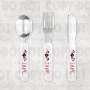 May include: A three-piece flatware set featuring a spoon, fork, and knife. Each piece has a white handle with a pink bat design and the name "JANE" in pink. The utensils are made of stainless steel.