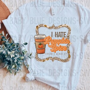 May include: A white t-shirt featuring the text "I Hate Pumpkin Spice" in orange and brown. The design includes a coffee cup with a pumpkin and a decorative frame.