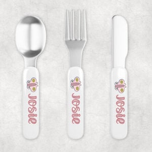 May include: A set of three personalized children's cutlery with white handles and stainless steel utensils. The handles feature a pink butterfly design and the name "Josie" in pink lettering.