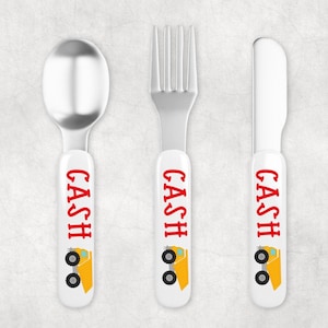 May include: A set of three personalized children's cutlery with a white handle and a yellow dump truck design. The handle is personalized with the name "CASH" in red letters.
