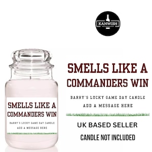 May include: A glass jar candle with a lid, labelled "Smells Like a Commanders Win." The label also states "Barry's Lucky Game Day Candle" and "Add a Message Here." The candle is a novelty item, perfect for gifting or personal use.