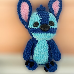 May include: A plush blue and light blue stuffed animal with large ears and black eyes. The stuffed animal has a textured, fuzzy appearance and is likely handmade. The ears have a pink interior. The toy is a character from a popular animated film.