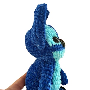 May include: A handmade blue and light blue crochet plush toy. The plush features large black eyes, a light blue belly, and dark blue ears. The toy is made of soft, textured yarn and is a character from a popular animated film.