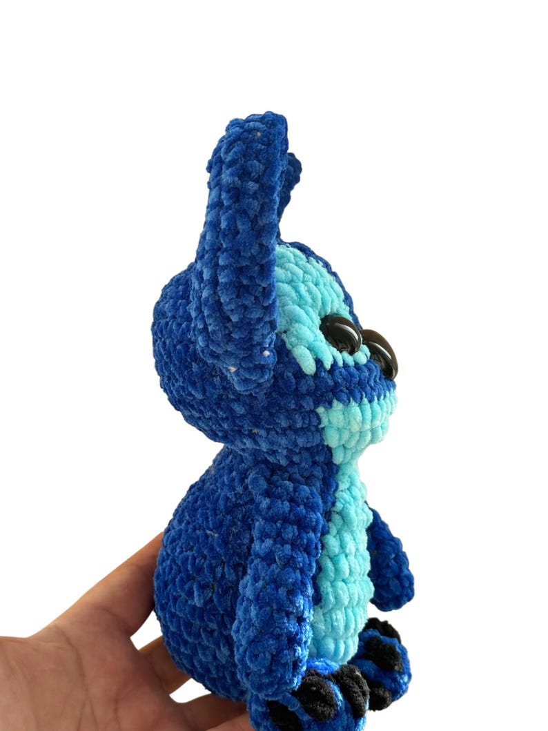 May include: A handmade blue and light blue crochet plush toy. The plush features large black eyes, a light blue belly, and dark blue ears. The toy is made of soft, textured yarn and is a character from a popular animated film.