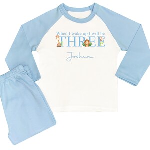 May include: A blue and white long-sleeved pajama set with a white shirt featuring the text "When I wake up I will be THREE" with animal illustrations and the name "Joshua" written below.