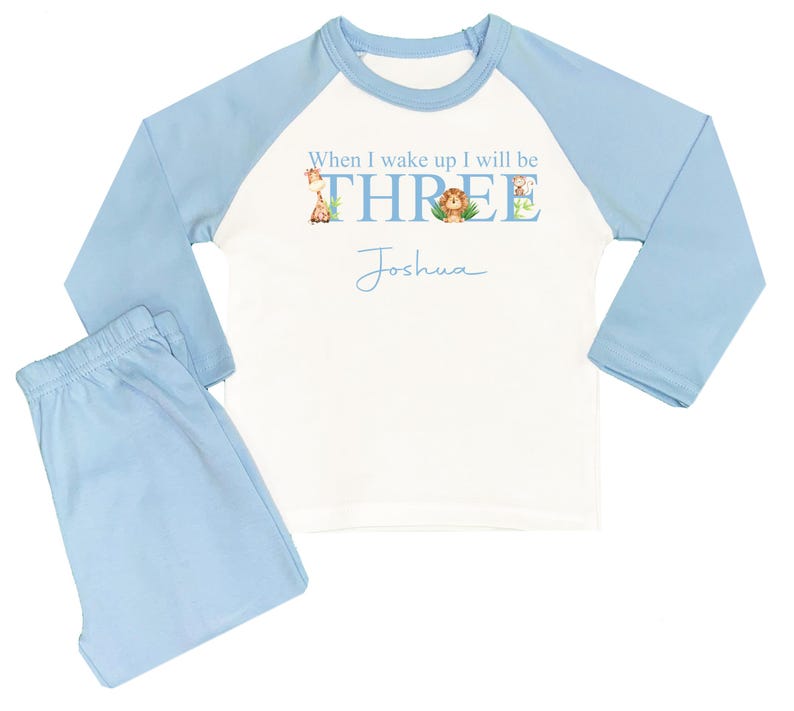 May include: A blue and white long-sleeved pajama set with a white shirt featuring the text "When I wake up I will be THREE" with animal illustrations and the name "Joshua" written below.