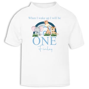 May include: White t-shirt with a blue and white rainbow, a giraffe, an elephant, and a lion. The text "When I wake up I will be ONE Finley" is printed on the shirt.