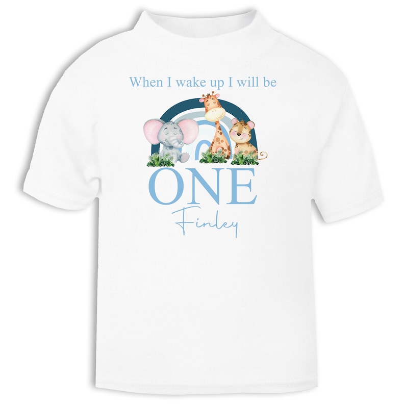 May include: White t-shirt with a blue and white rainbow, a giraffe, an elephant, and a lion. The text "When I wake up I will be ONE Finley" is printed on the shirt.