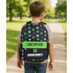 May include: Black backpack with a green and white Minecraft pattern. The backpack has a green top section with the name "GEORGE" in white block letters. The bottom section features the Minecraft logo.