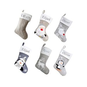 May include: Six personalised Christmas stockings with different characters and names. The stockings are in grey and white with a white cuff. The characters include Santa, a reindeer, a penguin, and a deer. The names on the stockings are Oliver, Elijah, and Rosie.
