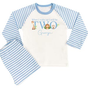 May include: White and blue striped pajamas with long sleeves. The top has a graphic of a giraffe, lion, and monkey with the text "When I wake up I will be TWO George".