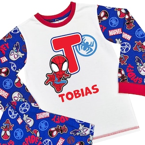 May include: A Spider-Man pyjama set in white and blue. The top has a red and blue Spider-Man graphic and the name "TOBIAS" in red. The sleeves and trousers feature a blue pattern with Spider-Man logos and the word "MARVEL".