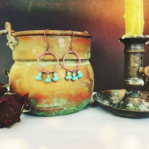 Puede incluir: Un par de pendientes de aro de cobre con cuentas turquesa que cuelgan de la parte inferior. Los pendientes se muestran en una olla de cobre con un fondo rústico.
