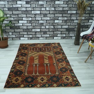 May include: A traditional prayer rug with a red center and intricate geometric patterns in shades of blue, brown, and gold. The rug has a fringed border and is perfect for use in a home or mosque.