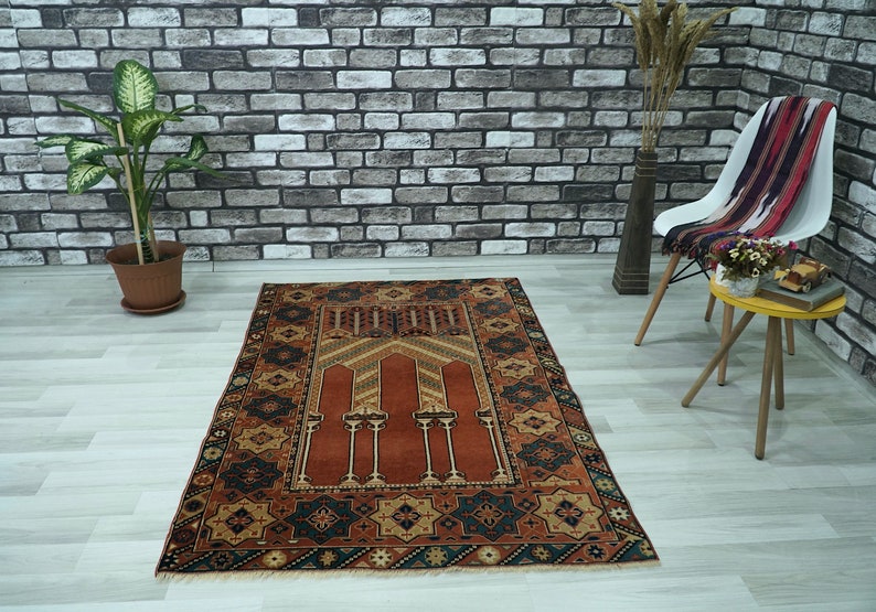 May include: A traditional prayer rug with a red center and intricate geometric patterns in shades of blue, brown, and gold. The rug has a fringed border and is perfect for use in a home or mosque.