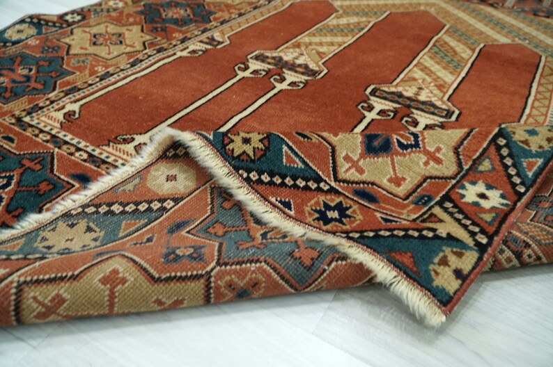 May include: A close-up of a folded rug with a red, orange, and blue geometric pattern. The rug has a fringe border and is made of wool.