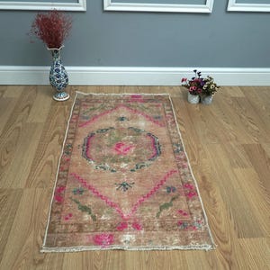 May include: A vintage Turkish rug with a pink, green, and brown floral pattern. The rug has a distressed look and is perfect for adding a touch of bohemian style to any room.