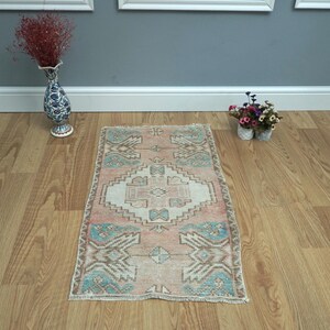 May include: A vintage Turkish rug with a light pink, cream, and blue geometric pattern. The rug is laid out on a wooden floor.