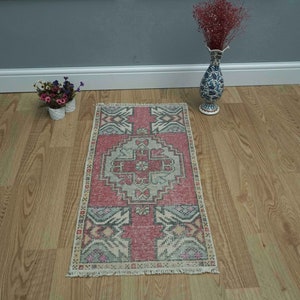 May include: A pink and cream vintage Turkish rug with a geometric pattern. The rug has a fringed edge and is laid out on a wooden floor.