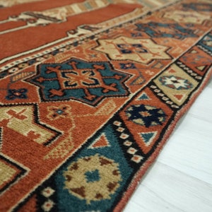 May include: Close-up of a red, blue, and beige patterned rug with intricate geometric designs. The rug has a fringed edge and is made of wool.