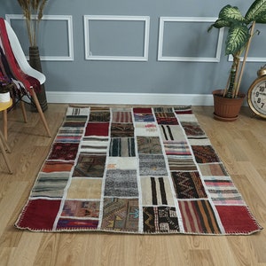 Op de afbeelding: Een rechthoekig patchwork vloerkleed met een verscheidenheid aan kleuren en patronen. Het vloerkleed bestaat uit talrijke rechthoekige stukken stof die aan elkaar zijn genaaid. De kleuren zijn onder meer rood, beige, bruin en blauw. Het vloerkleed is ongeveer 152 cm bij 213 cm.