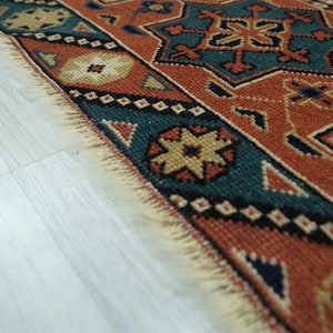May include: Close-up of the edge of a colorful rug with intricate geometric patterns in shades of red, blue, beige, and black. The rug has a fringe border.