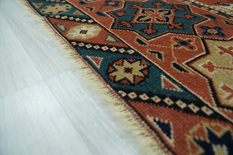 May include: Close-up of the edge of a colorful rug with intricate geometric patterns in shades of red, blue, beige, and black. The rug has a fringe border.