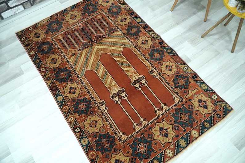 May include: A traditional prayer rug with a red center and intricate geometric patterns in shades of blue, green, and gold. The rug has a fringed border and is perfect for use in a home or mosque.