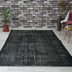May include: A large, rectangular black rug with a distressed, textured appearance. The rug has a faded, vintage look, with lighter grey areas creating a mottled effect. The rug is placed on a light-coloured floor.