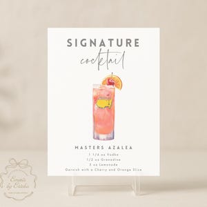 May include: A white sign with the words "SIGNATURE cocktail" and a watercolor illustration of a cocktail. The cocktail is pink and garnished with a cherry and orange slice. The sign reads "MASTERS AZALEA" with the ingredients listed.