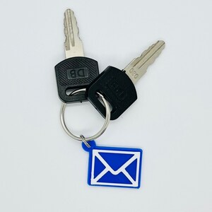Peut inclure: Deux cl&eacute;s argent&eacute;es avec des t&ecirc;tes en plastique noir attach&eacute;es &agrave; un porte-cl&eacute;s argent&eacute; avec un charme enveloppe bleu. Les cl&eacute;s portent les inscriptions "DB" et "080" sur les t&ecirc;tes.