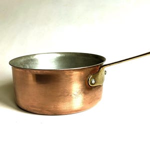 Peut inclure: Une casserole en cuivre avec une poignée et une fixation en laiton. L'intérieur de la casserole est argenté. La casserole est ronde et possède une seule longue poignée.