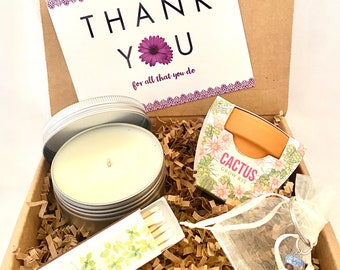 May include: A gift box filled with brown packing paper and a thank you card with purple flowers. The box contains a candle, matches, a cactus grow kit, and a small bag with a beaded keychain.