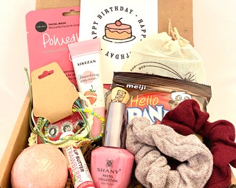 May include: A pink and brown gift box filled with various items, including a pink bath bomb, a pink nail polish bottle, a pink and green beaded bracelet, a pink and white lip butter, a pink and white body lotion, a brown and white bag, a brown and white snack bag, and a pink and brown hair scrunchie. The box also includes a pink and white face mask and a pink and white card with the text "Happy Birthday".