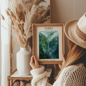 May include: A framed print of a watercolor painting depicting a lush green forest with a waterfall. The print has the text "FORKS - WASHINGTON - Population: 3,120 people" at the bottom.