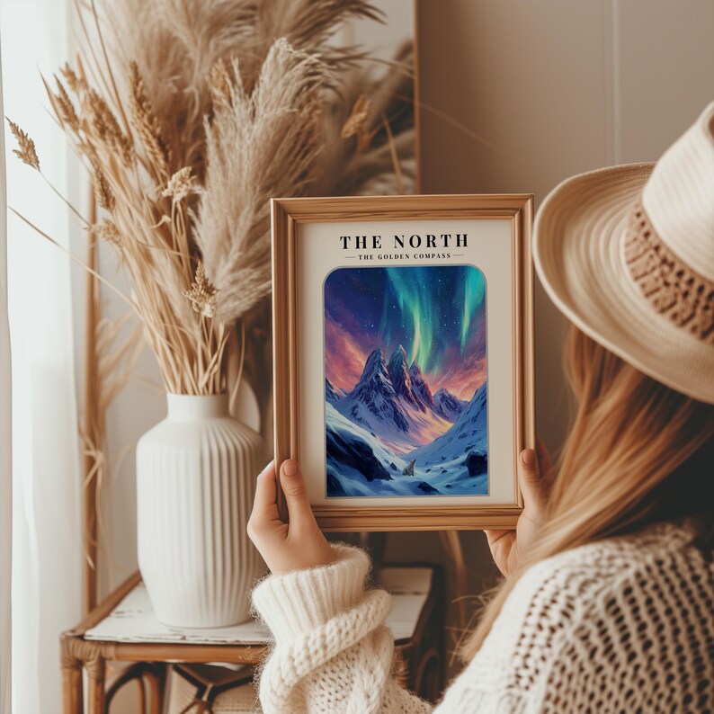 May include: A framed print with a mountain scene and a colorful aurora borealis in the sky. The text "THE NORTH - THE GOLDEN COMPASS" is at the top of the print.