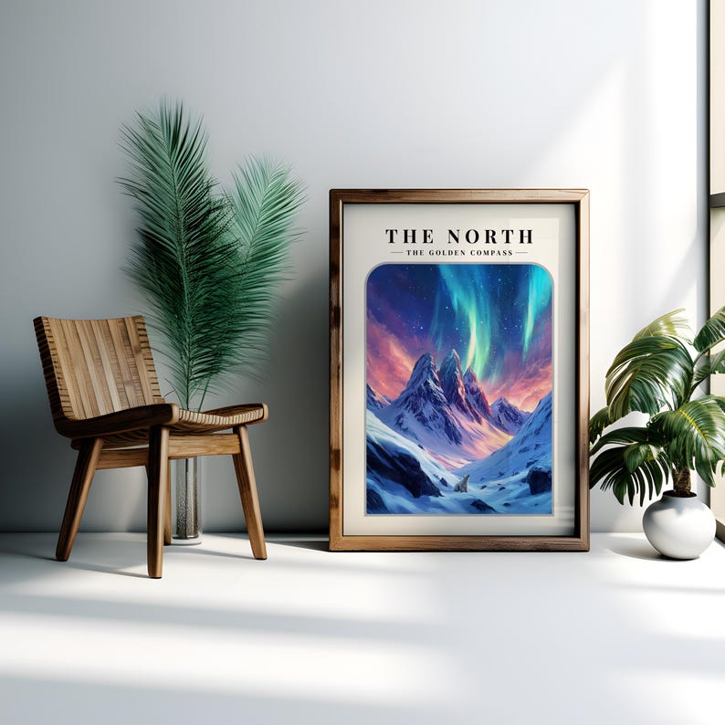 May include: A framed print with a mountain scene and the text "THE NORTH - THE GOLDEN COMPASS" at the top. The mountains are covered in snow and the sky is filled with a vibrant green and purple aurora borealis.