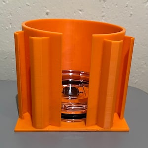 May include: Orange plastic cup holder with a clear glass cup inside. The holder has a base and vertical dividers.