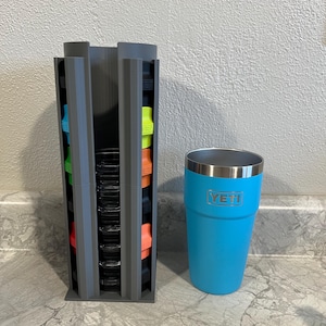 May include: A gray plastic organizer with multiple slots for storing colorful lids. A blue Yeti tumbler is next to the organizer on a gray countertop.