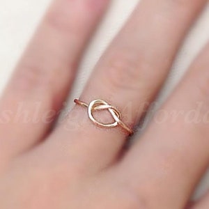 Puede incluir: Un anillo de nudo de oro simple. El anillo es delgado y delicado, con un diseño de nudo en el centro.