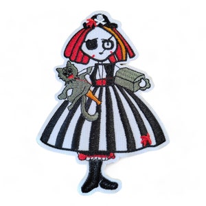 May include: Iron-on embroidered patch depicting a cartoon pirate girl with red hair, an eyepatch, and a striped dress. She is holding a small grey cat and a treasure chest.