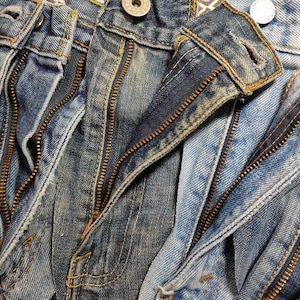 May include: Close-up of multiple pairs of blue denim jeans with gold zips. The zips are open and the denim is worn and faded.