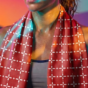 Pu&ograve; includere: Un asciugamano sportivo rosso con un motivo geometrico bianco, drappeggiato intorno al collo. La persona indossa un reggiseno sportivo grigio. Lo sfondo presenta un gradiente di rosa, arancione e blu. Ideale per l'esercizio.