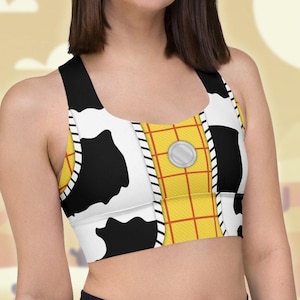 May include: A black and white cow print sports bra with a yellow and red plaid pattern on the front. The bra has a scoop neck and racerback style.